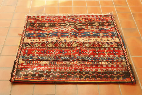 bedding bag made up of a fabric that is bands of brown, yellow, red and blue.  All of these have decoration stitched onto them.  The decoration is geometric in style and uses the same colour palette. 