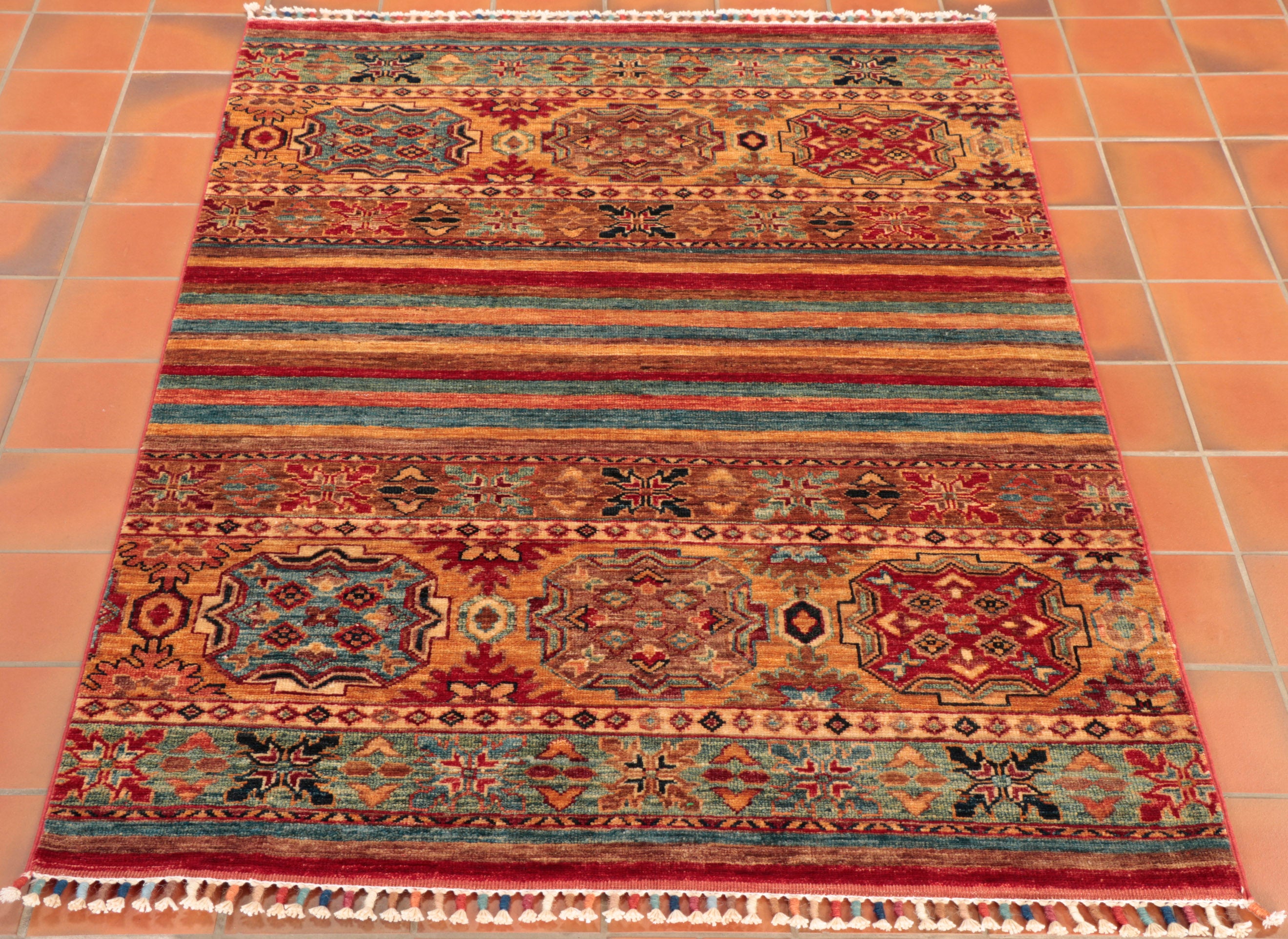 This bright and playful Fine Afghan Samarkand features a more modernistic, striped, centre that is top-and-tailed by traditional geometric patterning. The piece combines eye-catching colours of maya blue and golden-yellow with touches of contrasting scarlet red and complementing hints of delicate earthy browns.