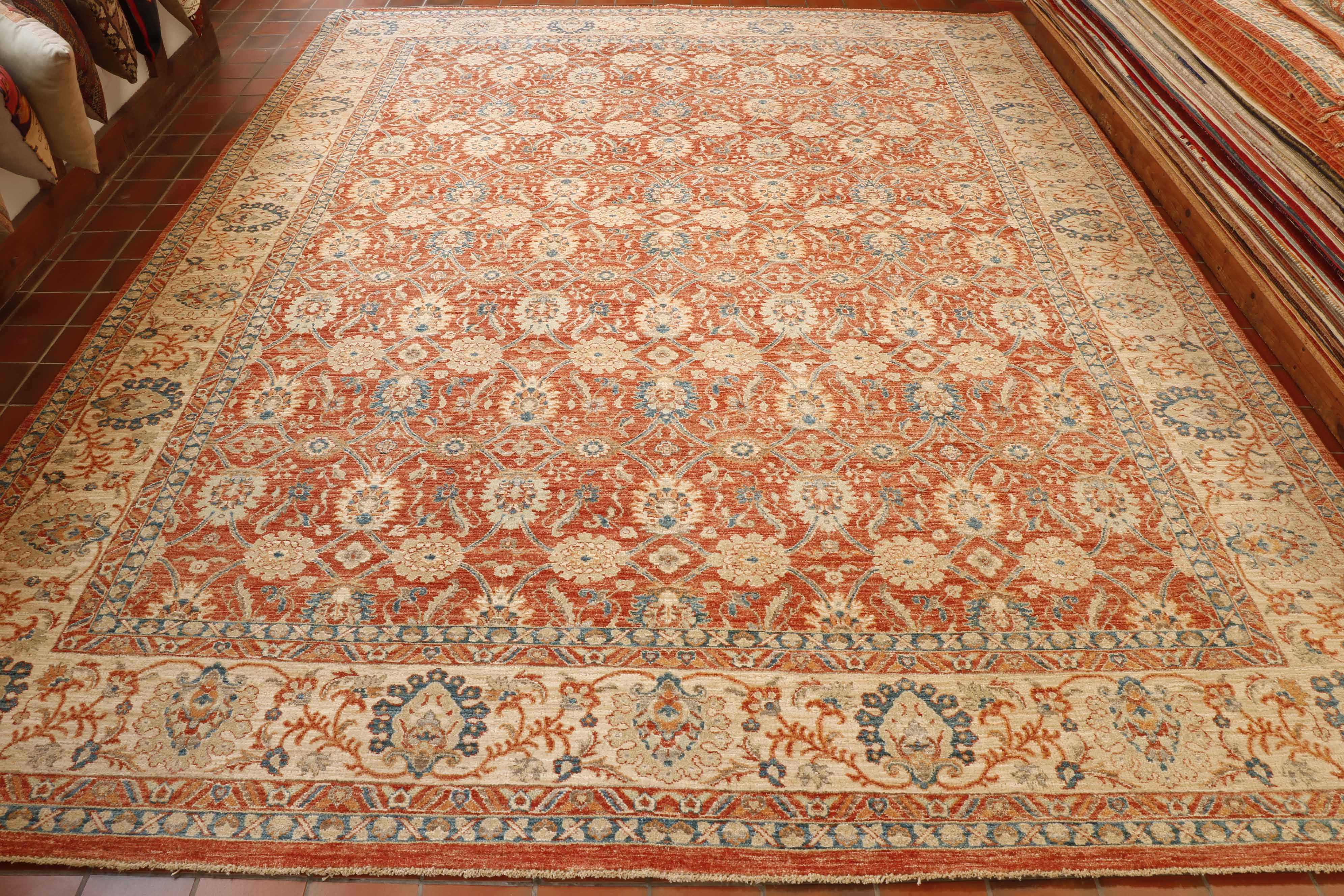 Soft terracotta ground with an intricate, connected network of floral designs using blue, cream and soft green.  There is a wide cream border with a  complimentary floral design using the terracotta, blue and green colours. 