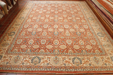 Soft terracotta ground with an intricate, connected network of floral designs using blue, cream and soft green.  There is a wide cream border with a  complimentary floral design using the terracotta, blue and green colours. 