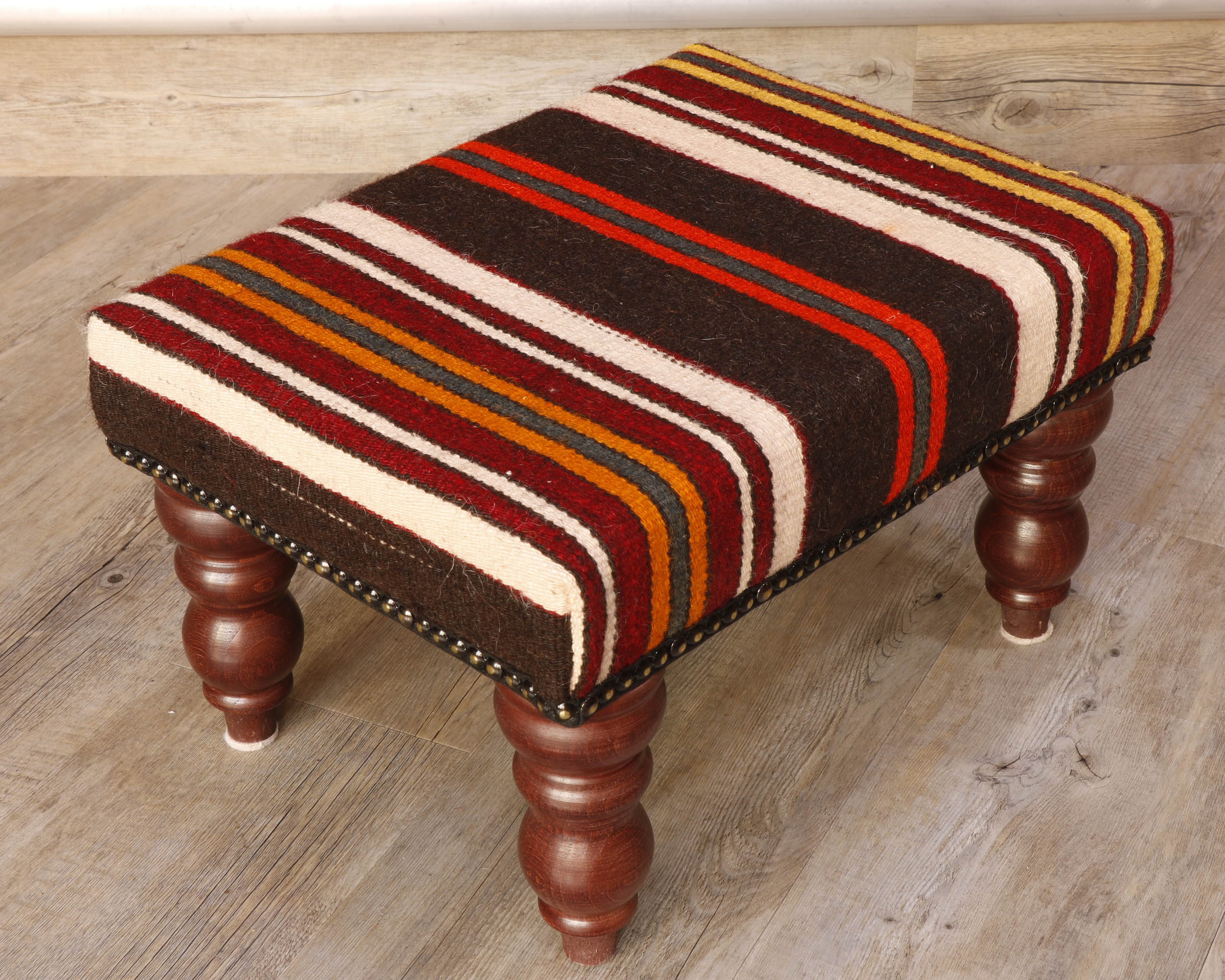 Theses Turkish Kilim stools often uses salvaged pieces.  This use produces an interesting look with the pattern being offset rather than centred, making the pieces unique and different.  This stool has bands of colour going across it’s width.  The colour palette for this stool is rich in Autumnal tones, oranges, browns, red, and ivory.  