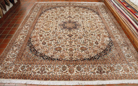 Intricate design of flora and fauna using terracotta, peach, cream and greens.  An area of deep blue that is oval within the main area of the rug.  There is a series of borders, some narrow and one wide with a cream ground.  